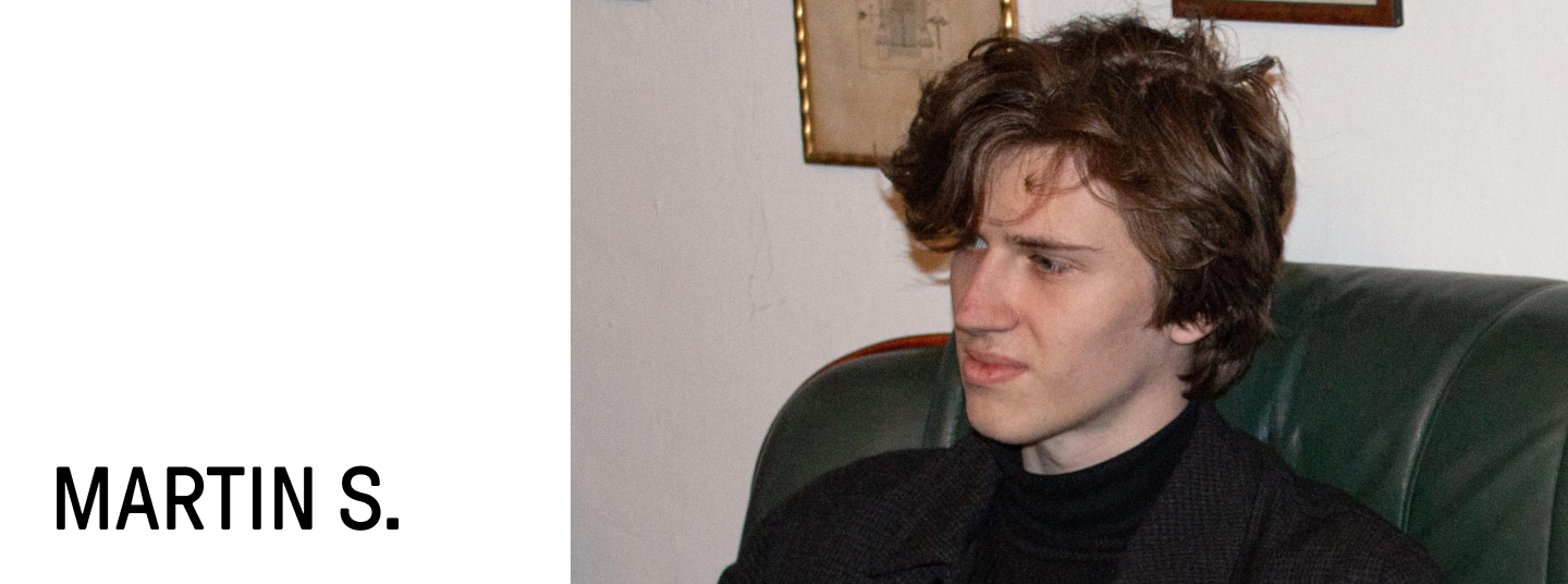 Martin is sitting on the couch, staring to his left.